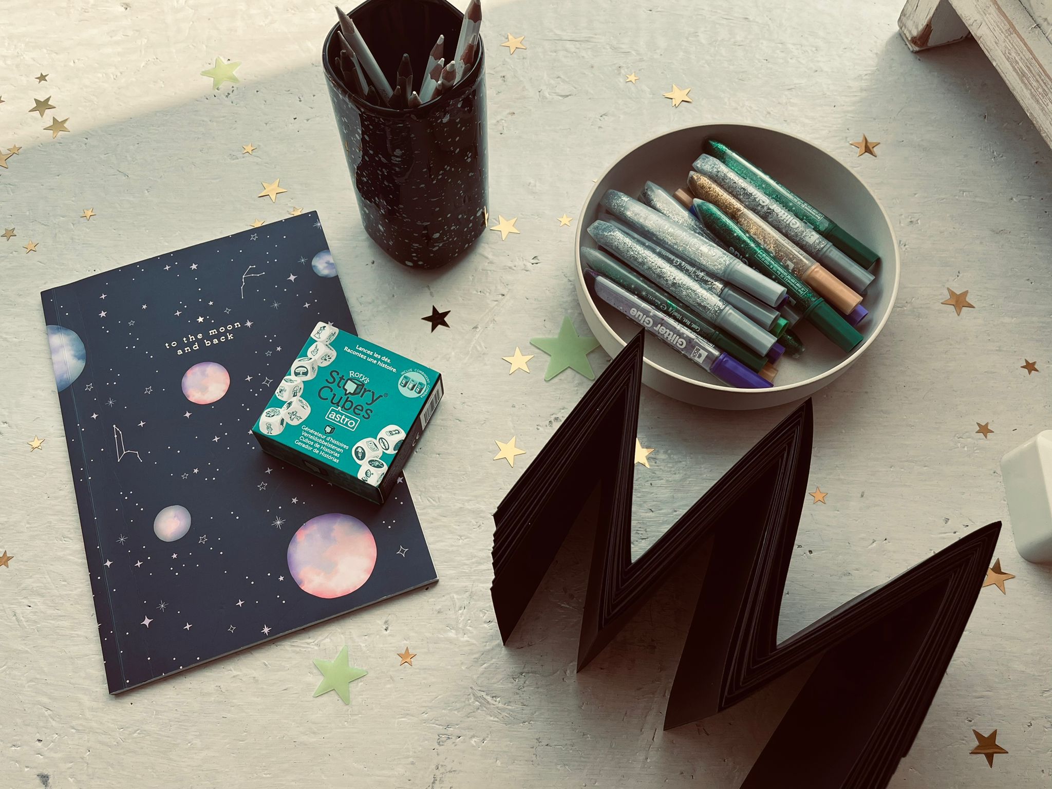 Een creatieve opstelling van een handgebonden boek, story cubes Astro en gouden sterren tijdens een workshop verhalen vertellen en boekbinden bij INKAMI Creative Studio