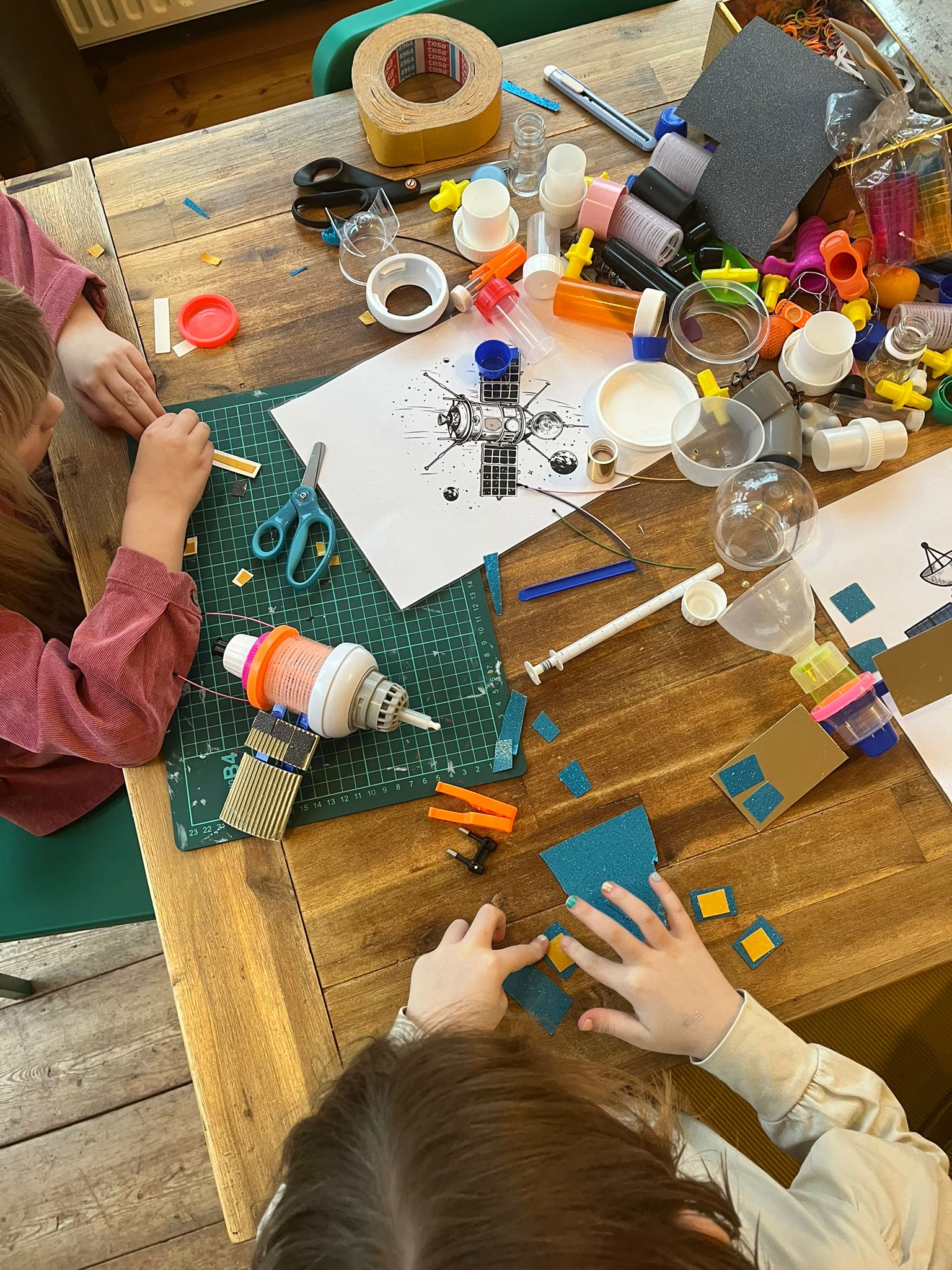 Kinderen bouwen met glitters en gerecycled materiaal satellieten tijdens een mixed-media workshop bij INKAMI Creative Studio in Den Helder